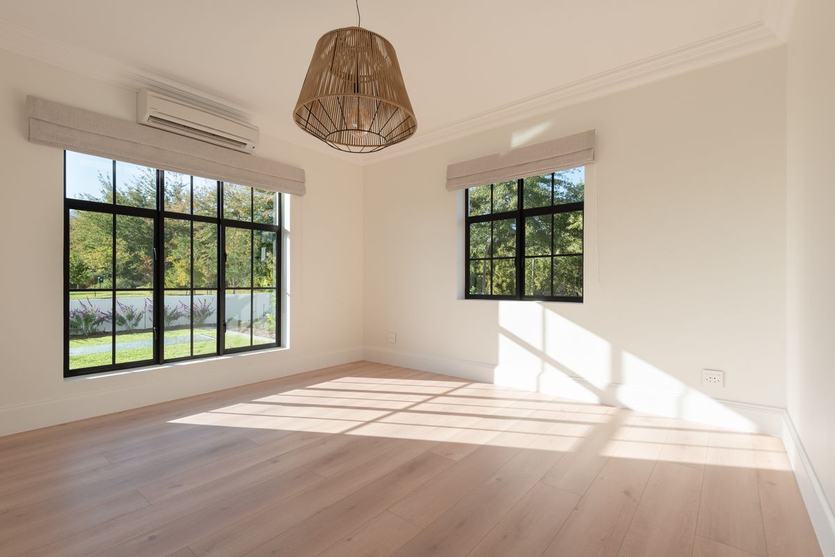 A bright, empty bedroom featuring light timber flooring, black-framed windows, and a wall-mounted air conditioning unit.