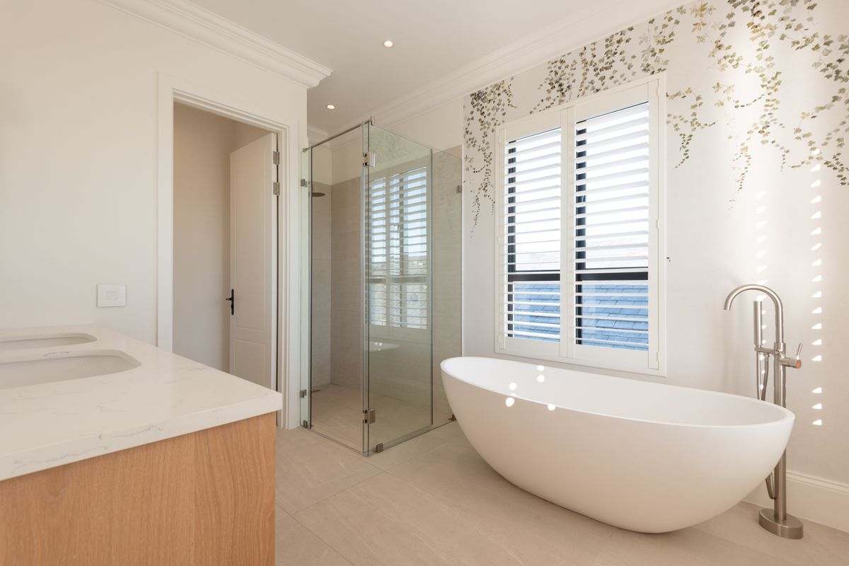 Modern bathroom featuring a freestanding bathtub, glass-enclosed shower, double vanity with stone countertop, and plantation shutters.