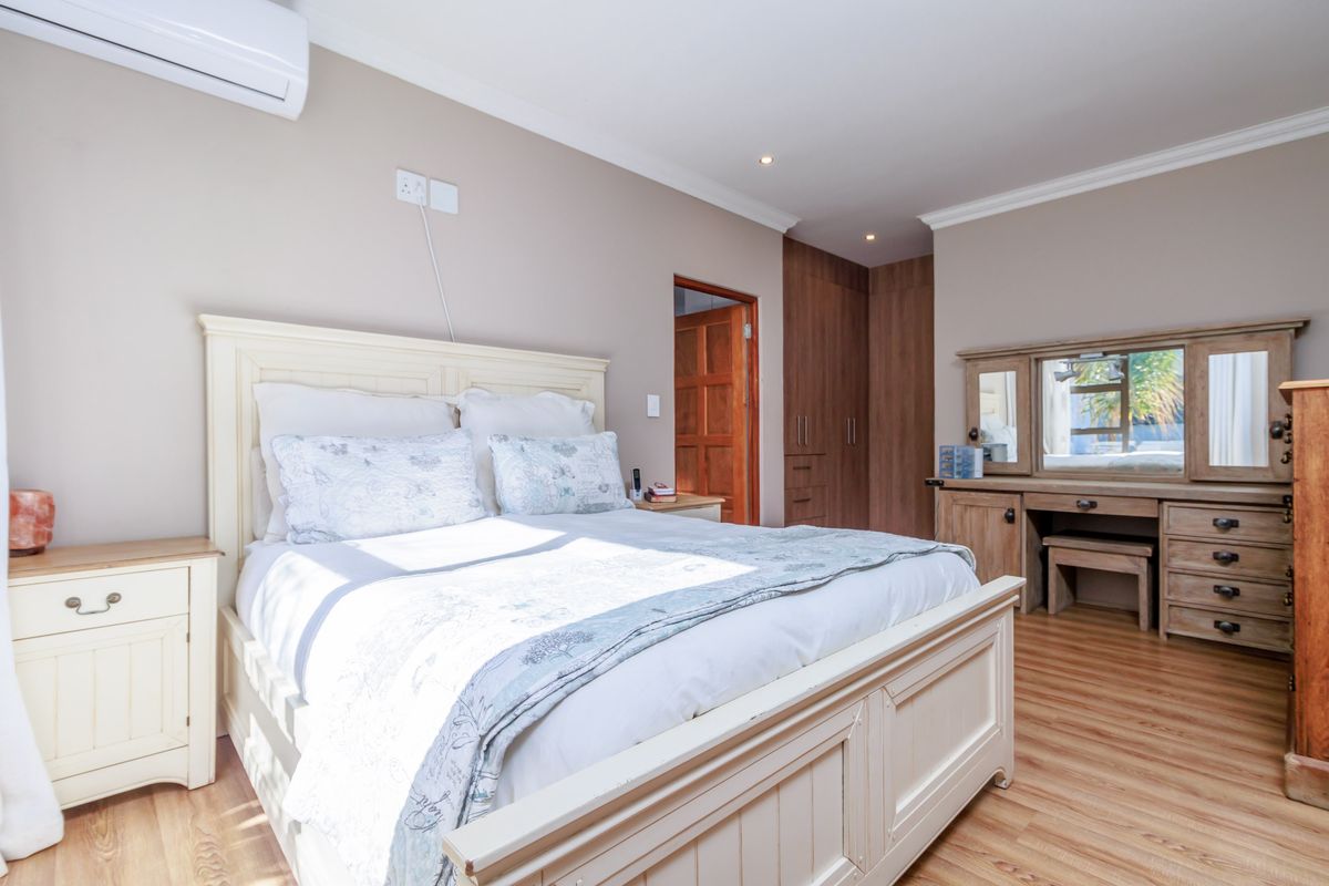 A well-maintained bedroom featuring wood-look flooring, built-in wooden cabinetry, and a wall-mounted air conditioning unit.