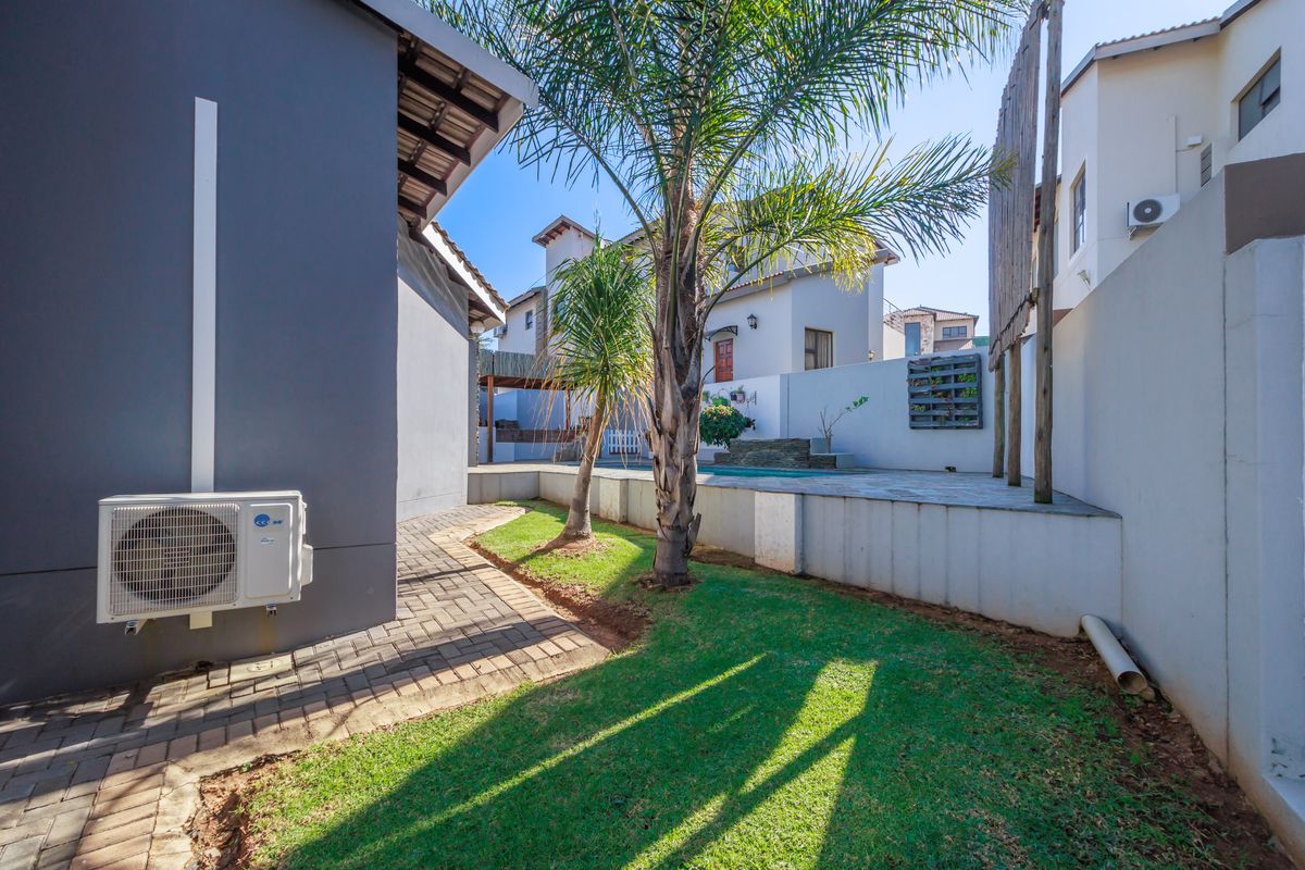 A private rear garden featuring a paved walkway, small lawn area, and a swimming pool with a stone water feature.