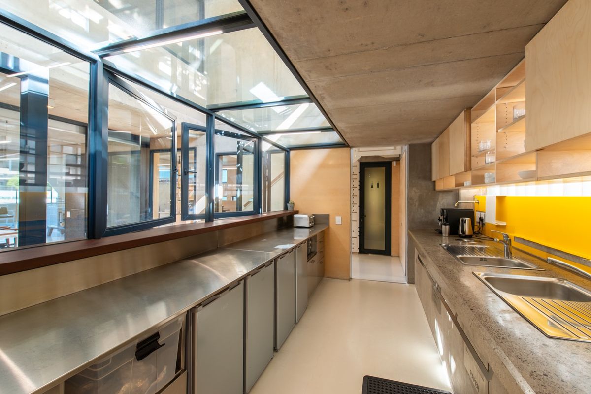 Modern industrial-style kitchen featuring stainless steel countertops, concrete ceiling, extensive glass skylights, and vibrant yellow tiled splashback with integrated cabinetry.
