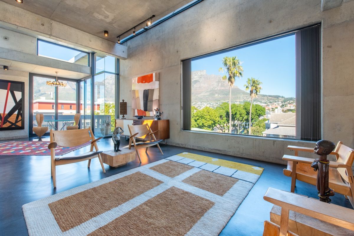 Spacious living area featuring exposed concrete walls and ceilings, polished concrete floors, and expansive windows offering panoramic mountain and city views.