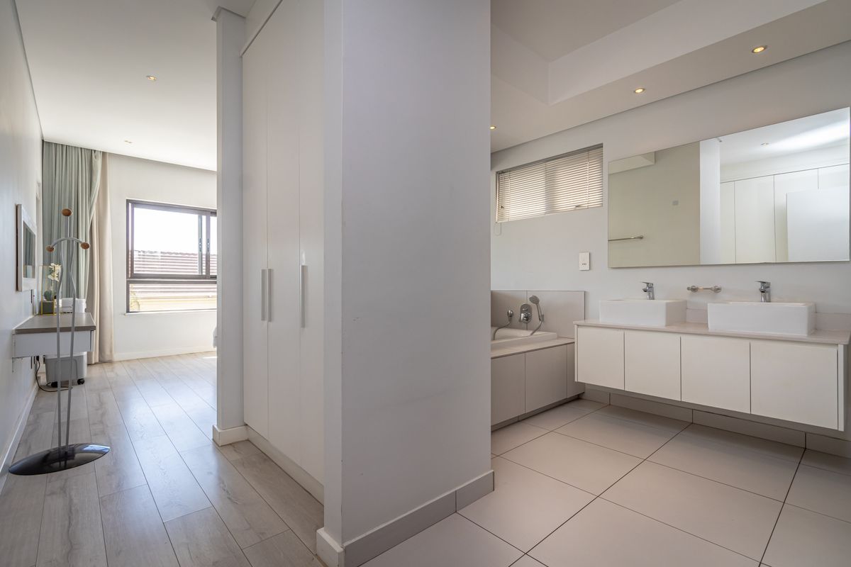 Modern open-plan bathroom and dressing area featuring a double vanity, built-in bathtub, and integrated cabinetry with neutral finishes.