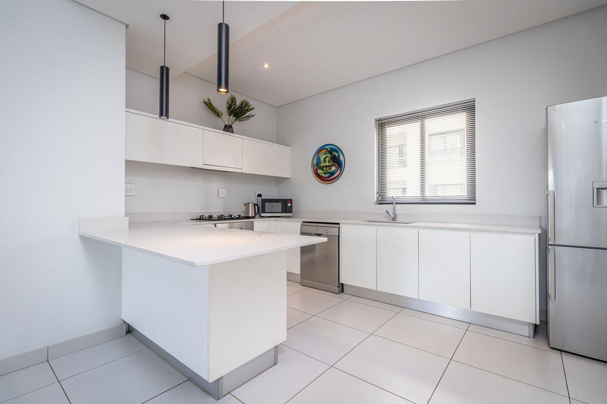 Modern kitchen featuring white cabinetry, stone countertops, a breakfast bar, integrated sink, and tiled flooring in a clean, minimalist design.