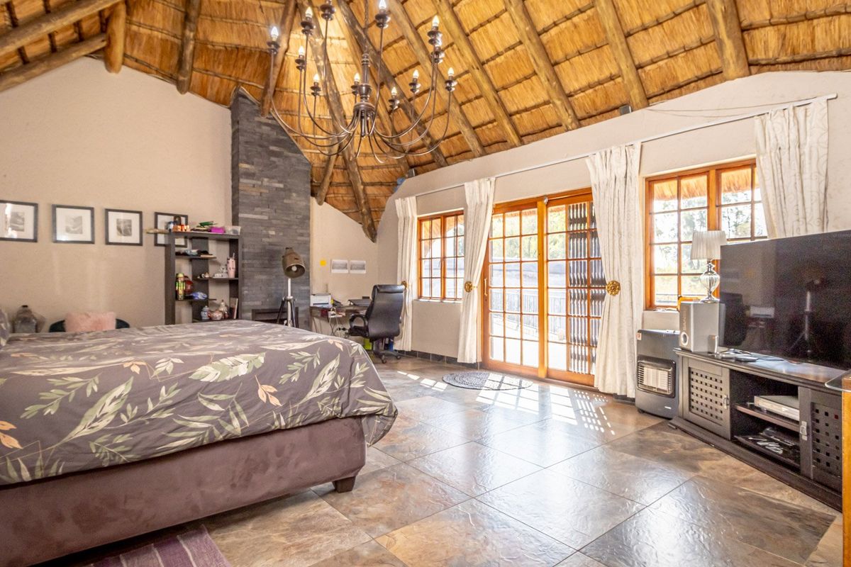 Spacious bedroom featuring a high vaulted thatched ceiling, exposed timber beams, stone-clad fireplace, and large glass sliding doors opening to the exterior.