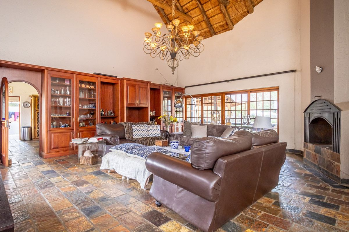 Spacious living room featuring a high vaulted thatched ceiling, built-in wooden cabinetry, stone tile flooring, and a traditional fireplace.