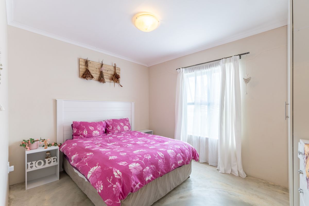 A well-lit bedroom featuring a built-in wardrobe, polished concrete flooring, and a large window with curtain rod.