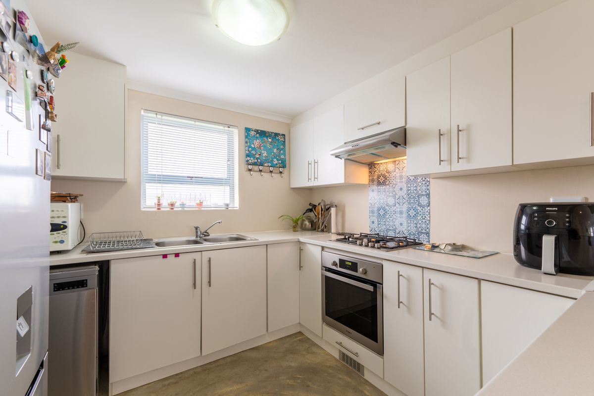 A functional kitchen featuring white cabinetry, a built-in oven, gas hob, extractor fan, and a decorative tiled splashback.