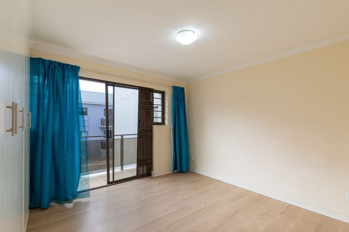 A bright bedroom featuring light wood-look flooring, built-in cupboards, and a sliding glass door providing access to a private balcony.