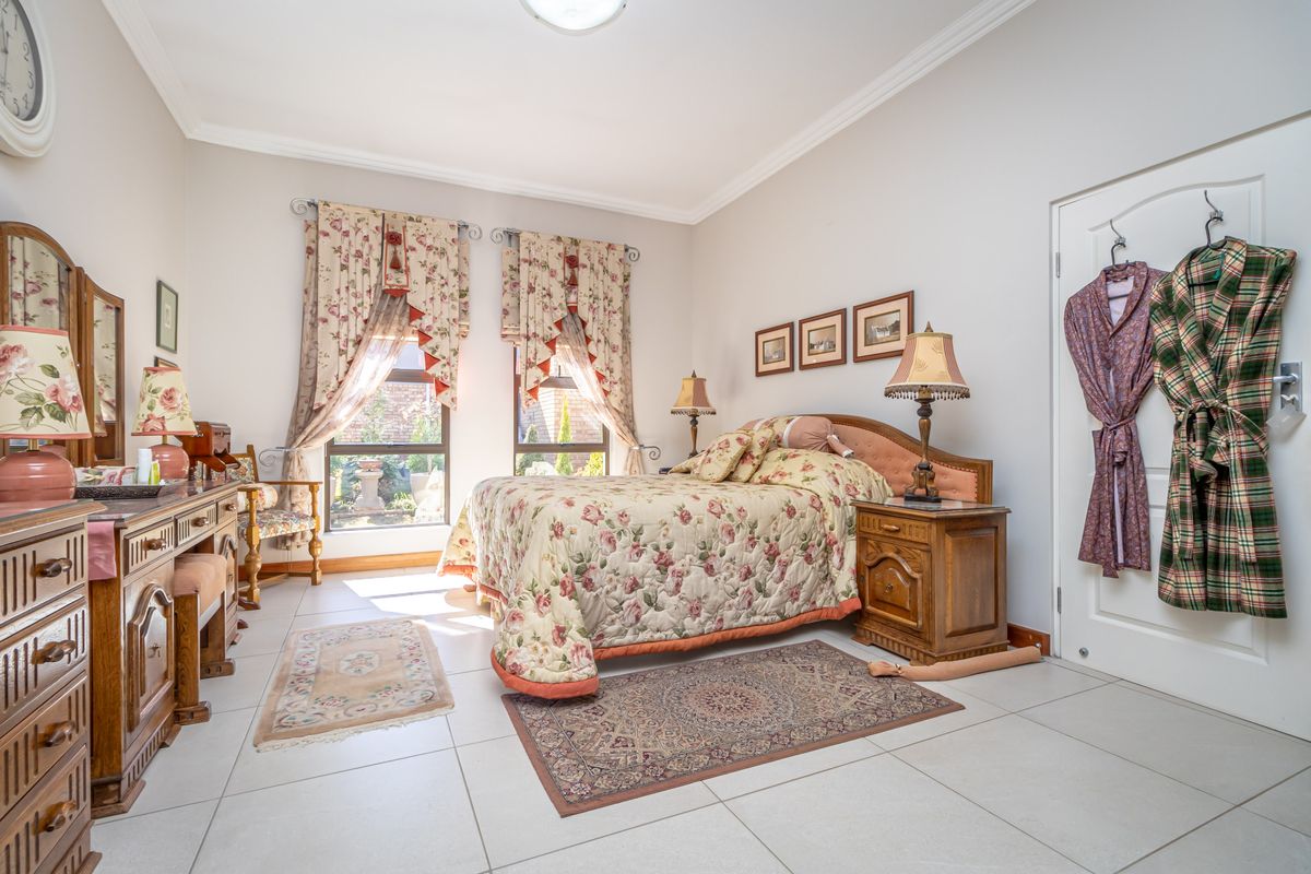A well-lit bedroom featuring neutral tiled flooring, crown molding, and large windows that provide natural light and a view of the garden.
