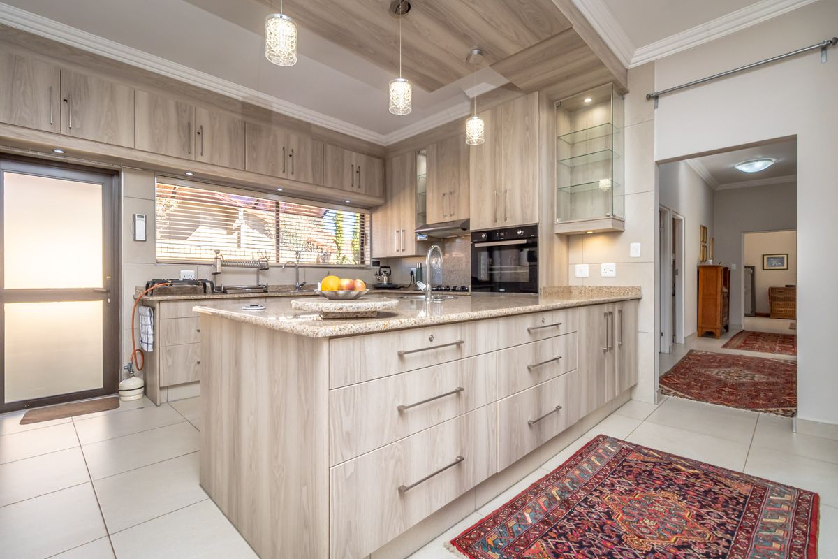 Modern kitchen featuring light wood cabinetry, granite countertops, a central island, built-in oven, and integrated glass display shelving.