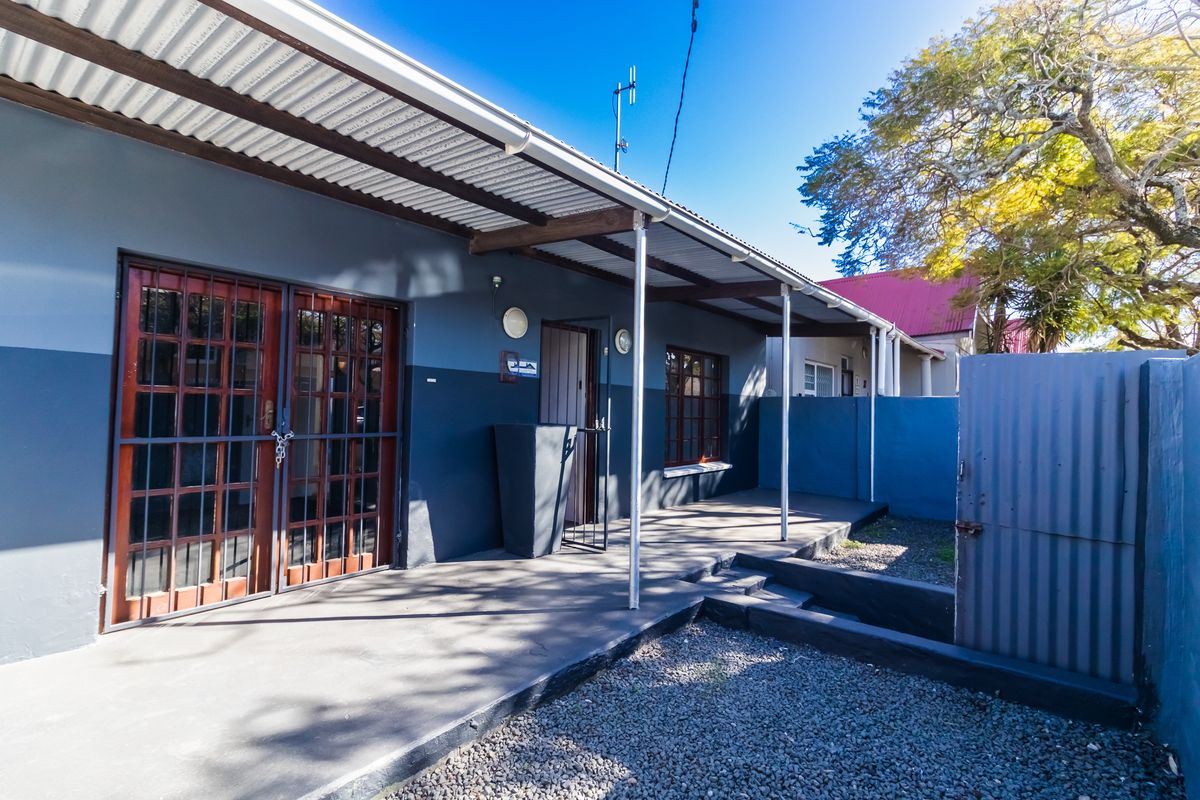 A covered patio area featuring a concrete floor, timber-framed glass doors, and a corrugated metal roof, providing a functional outdoor transition space.
