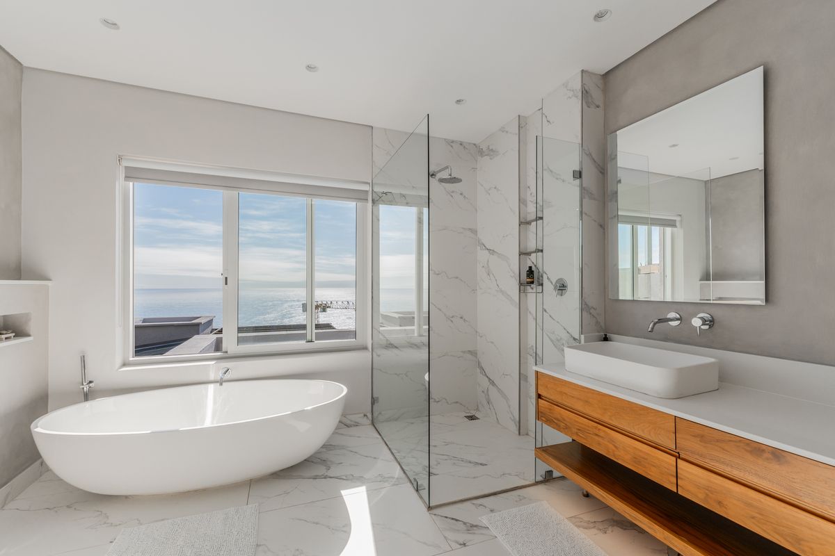 Modern bathroom featuring a freestanding bathtub, glass-enclosed walk-in shower, marble-look tiling, and a floating wooden vanity with a vessel sink.