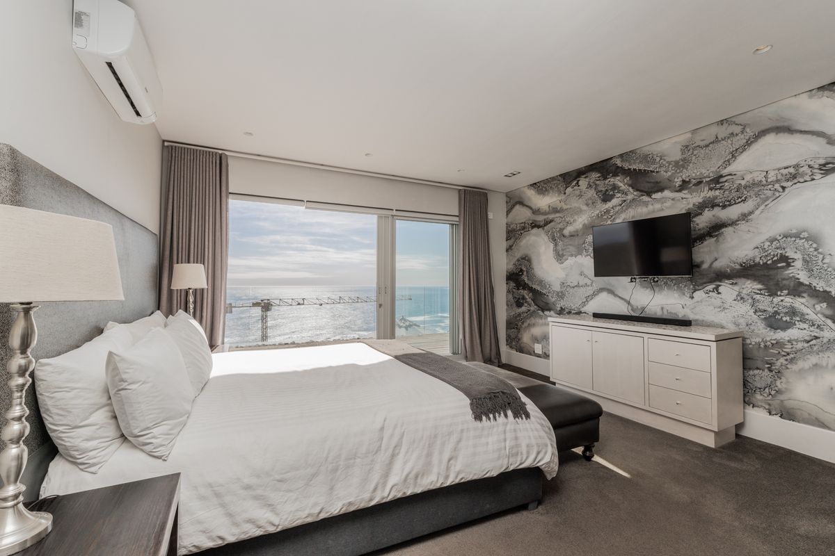 Spacious bedroom featuring a large sliding glass door with ocean views, wall-mounted air conditioning unit, and a feature wall with decorative wallpaper.