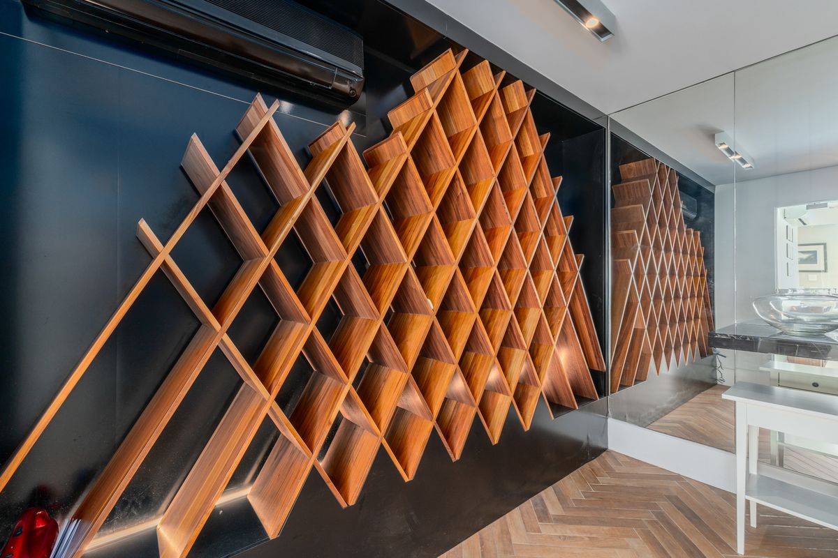 A modern interior space featuring a striking custom wooden geometric wall shelving unit set against a sleek black panel with herringbone wood flooring.
