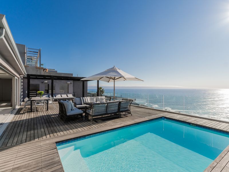 Spacious outdoor deck featuring a swimming pool, glass balustrades, and expansive ocean views, perfect for coastal entertaining.