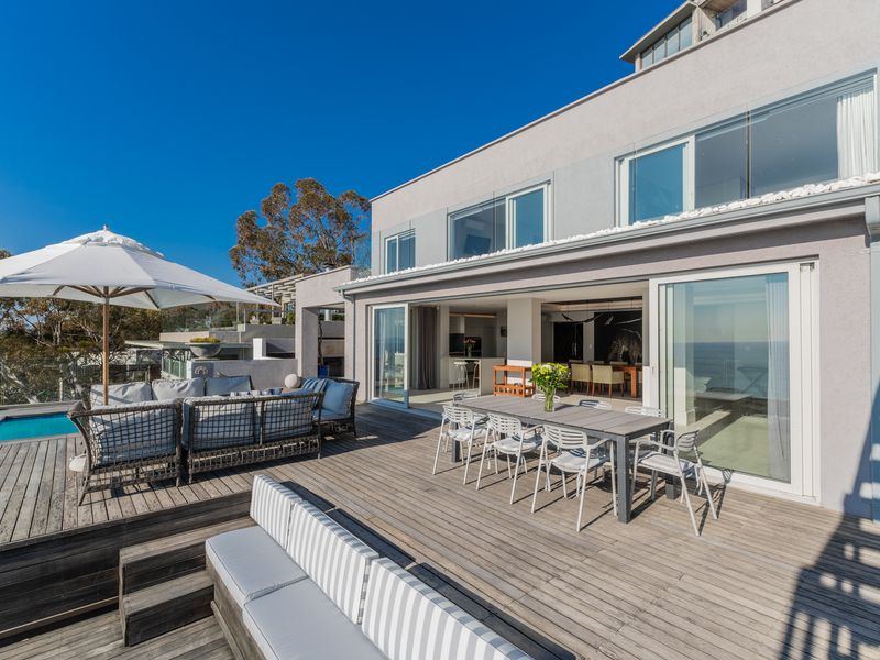 Spacious outdoor timber deck featuring a swimming pool, integrated seating, and seamless flow into the open-plan living and dining area through large sliding doors.