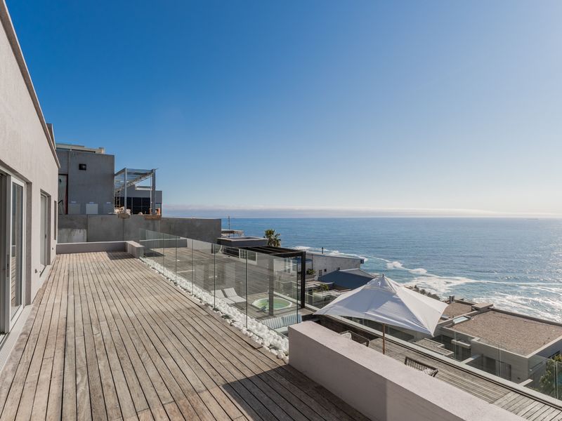 Spacious outdoor terrace featuring timber decking and glass balustrades, offering expansive ocean views and direct access to the interior living space.