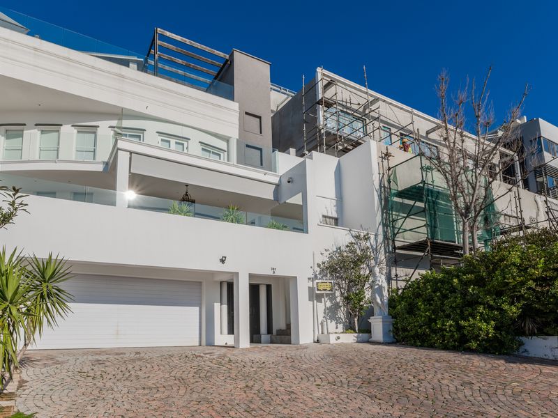 Front elevation of a multi-level residence featuring a paved driveway, integrated garage, and balconies, currently undergoing exterior maintenance and construction.
