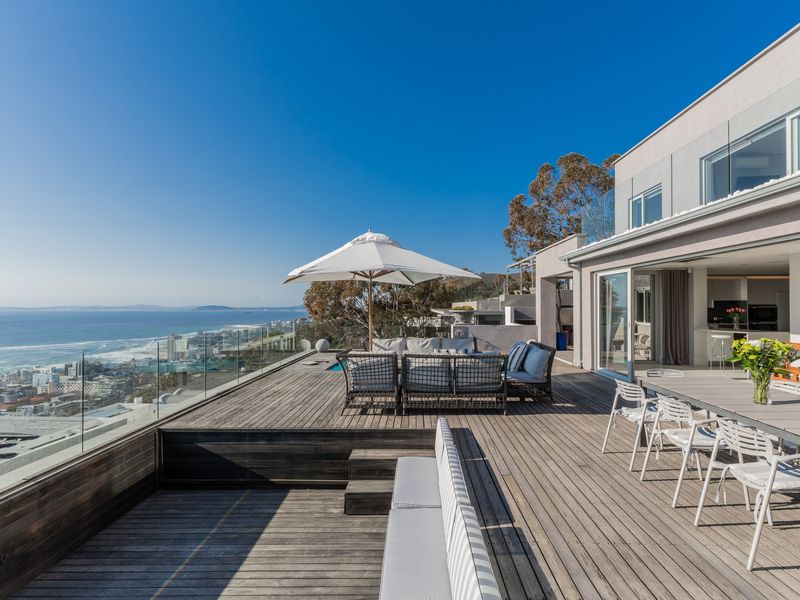 Expansive outdoor timber deck featuring a glass balustrade, integrated seating, and stunning coastal views, seamlessly connected to the indoor living area.
