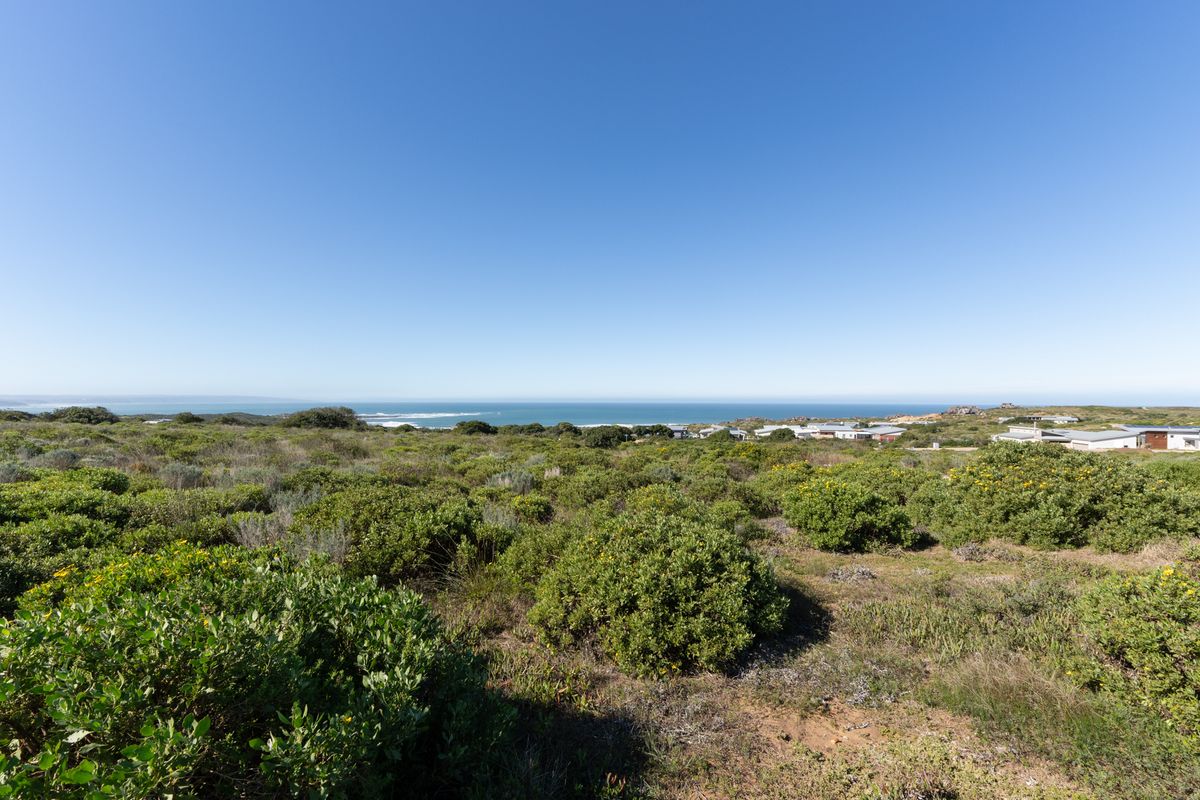 A wide-angle view of the vacant residential land featuring natural coastal vegetation and a clear horizon line overlooking the ocean.