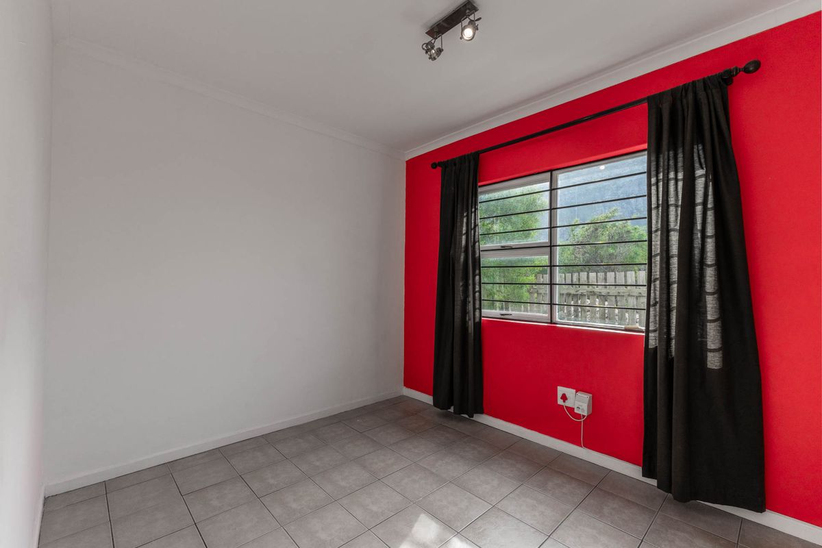 An empty bedroom featuring tiled flooring, a bold red accent wall, and security bars on the window.