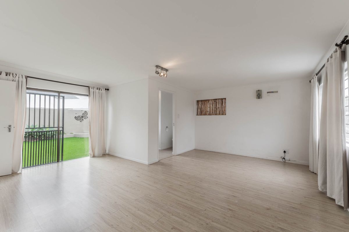 Bright and spacious living area featuring light-toned laminate flooring, neutral walls, and a sliding glass door providing direct access to the rear garden.