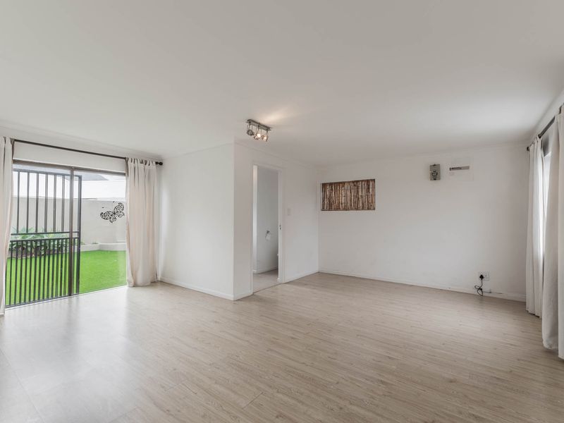 Bright and spacious living area featuring light-toned laminate flooring, neutral walls, and a sliding glass door providing direct access to the rear garden.