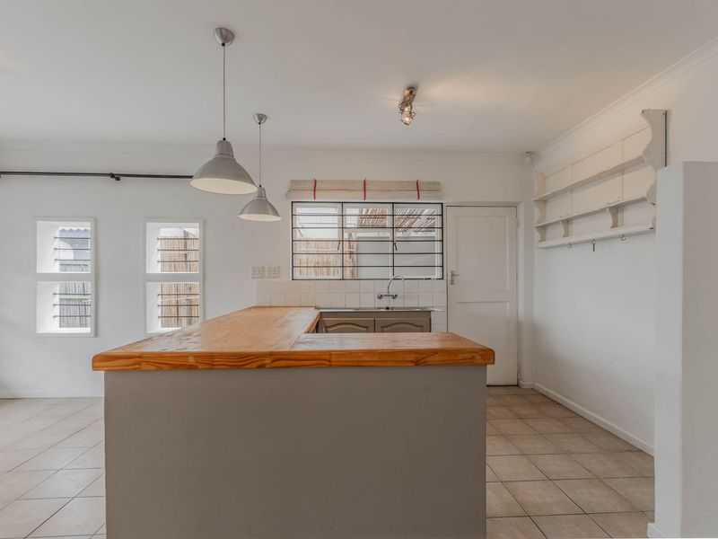 A bright, open-plan kitchen featuring a central island with a wooden countertop, tiled flooring, and built-in wall shelving.