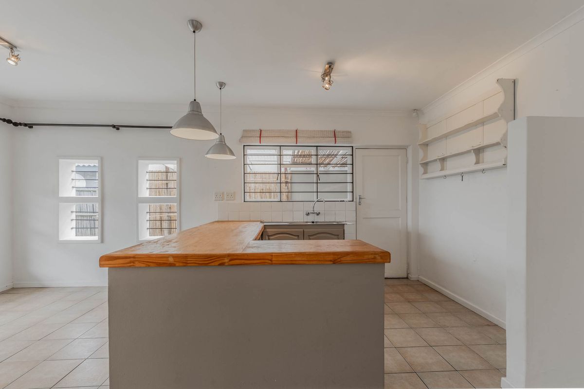 A bright, open-plan kitchen featuring a central island with a wooden countertop, tiled flooring, and built-in wall shelving.