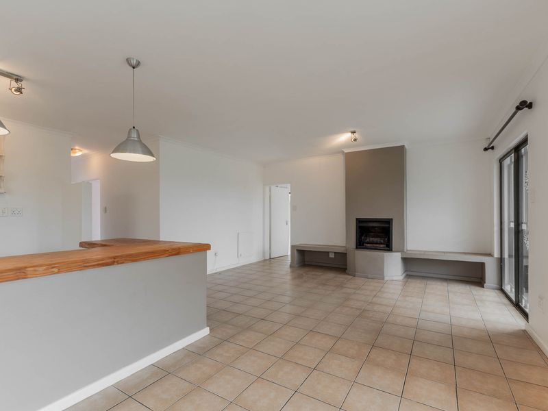 Spacious open-plan living area featuring tiled flooring, a built-in fireplace with bench seating, and a breakfast bar, leading to a sliding glass door.
