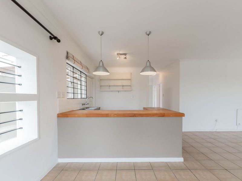 An open-plan living and kitchen area featuring a breakfast bar with a wooden countertop, tiled flooring, and neutral finishes.