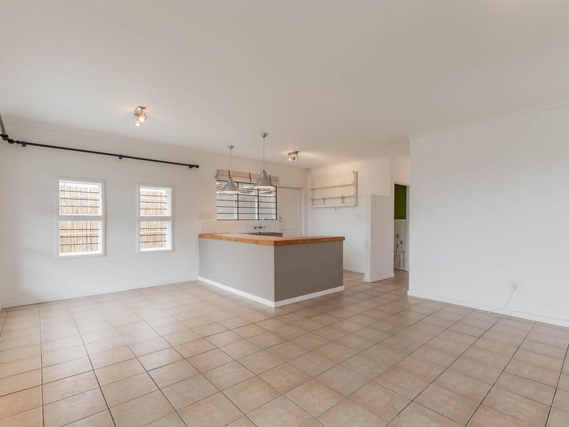 An open-plan living and kitchen area featuring tiled flooring, a central kitchen island with a wooden countertop, and ample natural light.