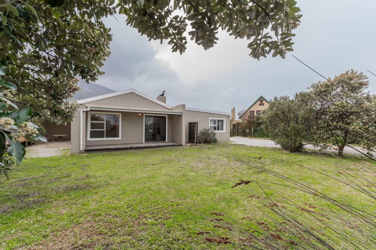 Rear view of the property featuring a covered patio, sliding glass doors, and a spacious lawn area under an overcast sky.
