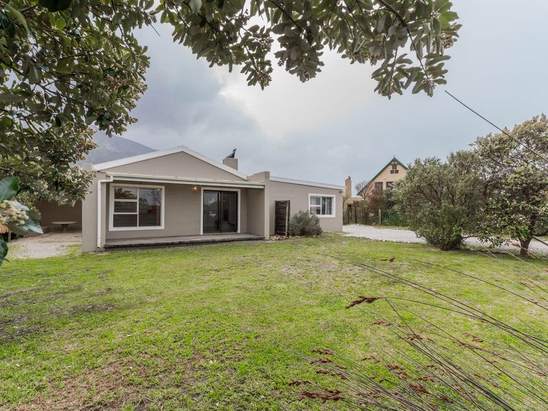 Rear view of the property featuring a covered patio, sliding glass doors, and a spacious lawn area under an overcast sky.