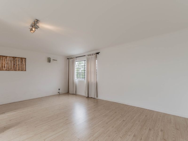 A bright and spacious living area featuring light-toned laminate flooring, neutral walls, and a window fitted with security bars.