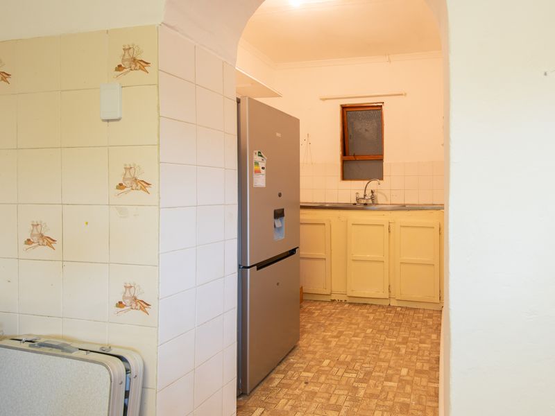 A functional scullery area featuring built-in cabinetry, a sink, and tiled splashbacks, accessible through a classic arched doorway.