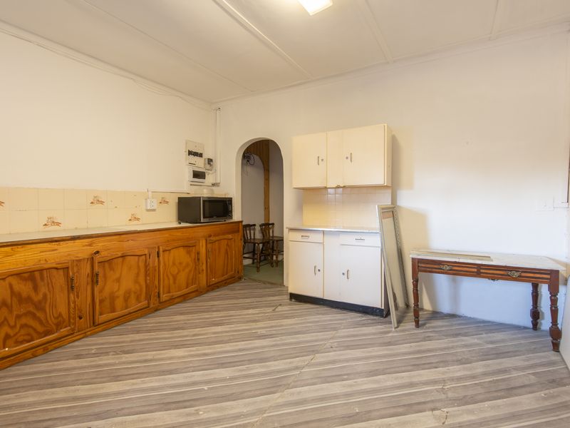 A dated kitchen space featuring wooden cabinetry, tiled backsplash, and an archway leading to an adjacent room, offering potential for a modern renovation.