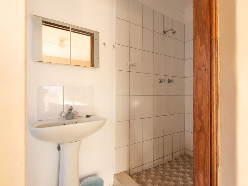 A functional bathroom featuring a pedestal basin, medicine cabinet, and a tiled shower enclosure with wall-mounted fixtures.