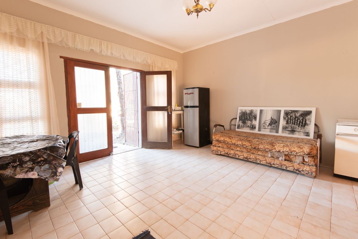 A living area featuring tiled flooring and double wooden doors providing access to the exterior, with neutral wall tones and a central ceiling light.