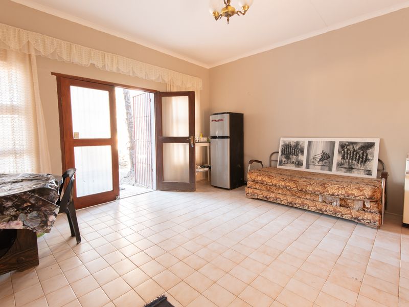 A living area featuring tiled flooring and double wooden doors providing access to the exterior, with neutral wall tones and a central ceiling light.