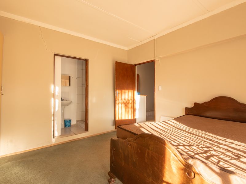 A bedroom featuring carpet flooring, a built-in wardrobe, and an attached en-suite bathroom, showing visible wall cracks requiring maintenance.