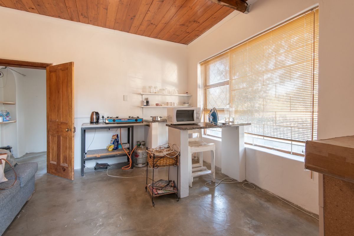 A rustic kitchen area featuring exposed timber ceilings, concrete flooring, and a built-in masonry counter with basic prep space.