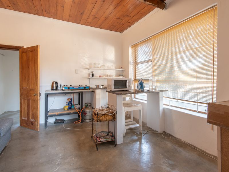A rustic kitchen area featuring exposed timber ceilings, concrete flooring, and a built-in masonry counter with basic prep space.