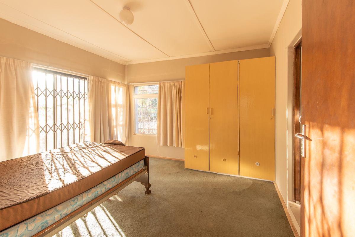 A bedroom featuring built-in cupboards, security gates on windows, and carpeted flooring, offering a functional space with potential for modernization.