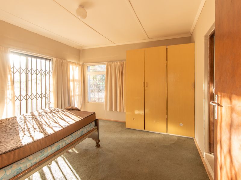 A bedroom featuring built-in cupboards, security gates on windows, and carpeted flooring, offering a functional space with potential for modernization.