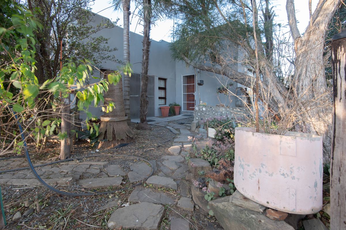 Rear exterior view of the property featuring a stone pathway leading to the entrance, surrounded by mature trees and garden landscaping.