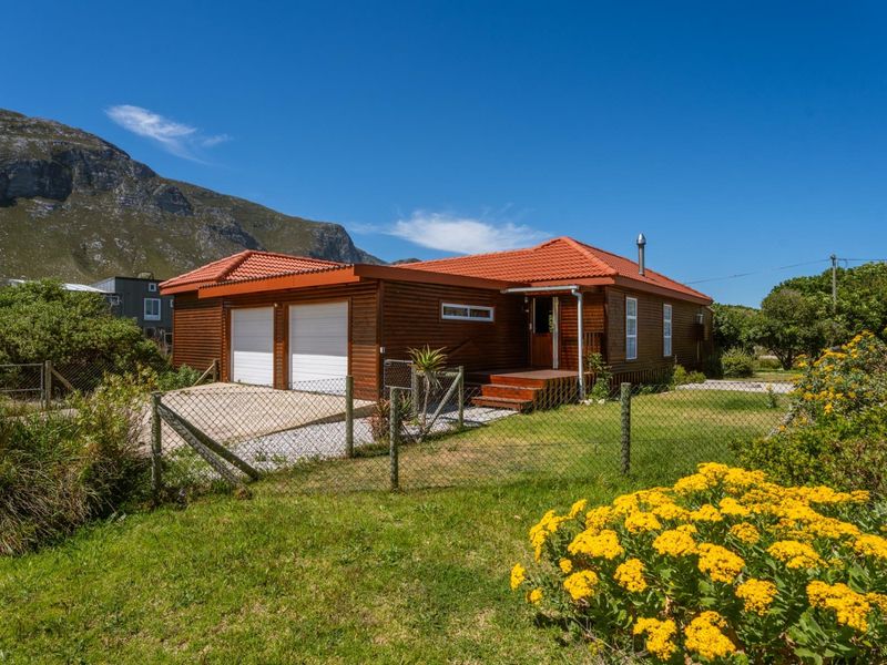 A well-maintained timber-clad house featuring a double garage, tiled roof, and a front timber deck, set within a fenced garden with mountain views.