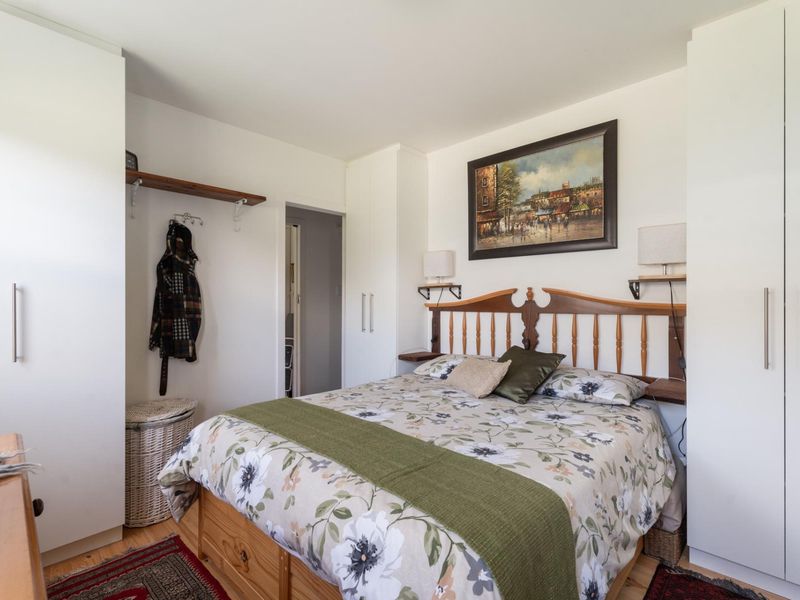 A well-maintained bedroom featuring built-in wardrobes, timber flooring, and wall-mounted shelving, offering a functional and comfortable living space.