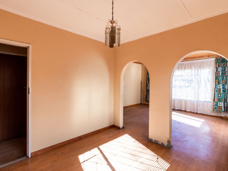 An empty living area featuring distinctive arched doorways, wooden flooring, and a classic pendant light fixture, offering a blank canvas for renovation.